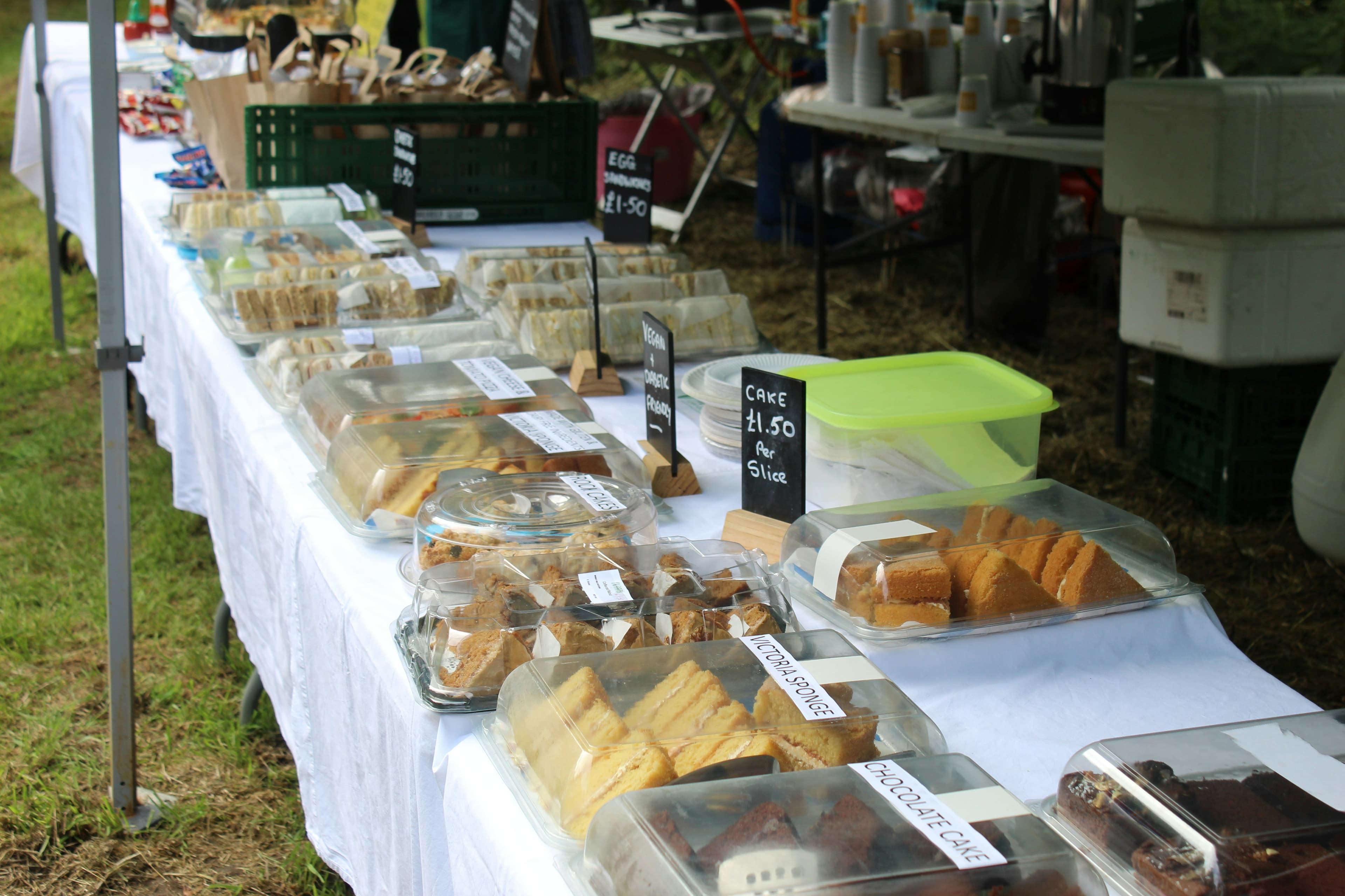 Outdoor bake sale table with wrapped cakes, traybakes and handwritten price signs